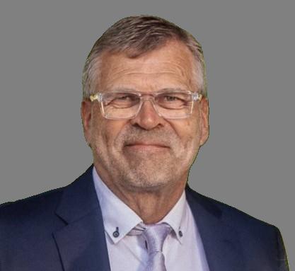 Harmaahiuksinen mies hymyilee kameraan, hänellä on silmälasit, puku ja vaalea solmio.