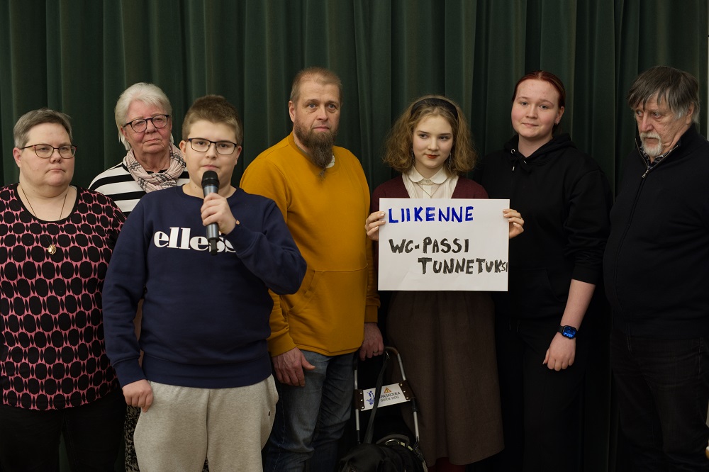 Vasemmalta oikealle seitsemän vaikuttajaa: Hanna Gröhn, Anja Lukjanov, Valtteri Tiirikainen, Petri Huttunen, Salla Österman pitelee käsissään kylttiä jossa lukee liikenne ja wc-passi, hänestä oikealla Sara Toiviainen ja Stig Strandberg.