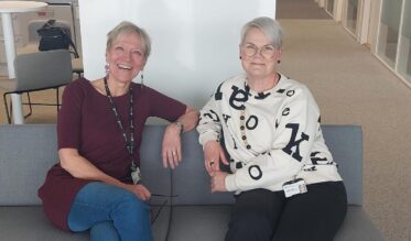 Kaksi henkilöä istuvat sohvalla ja katsovat hymyillen kameraan.