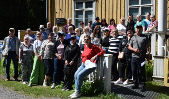 Joukko ihmisiä keltaisen puutalon edustalla.