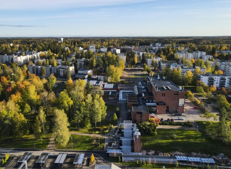 Ilmakuva Järvenpäästä syksyisessä maisemassa. Kuvassa näkyy kaupungin keskusta-alue kerrostaloineen, Järvenpään kirjasto ja kulttuuritalo, sekä ympäröivää puustoa, jossa syksyn värit vaihtelevat vihreästä keltaiseen ja oranssiin.