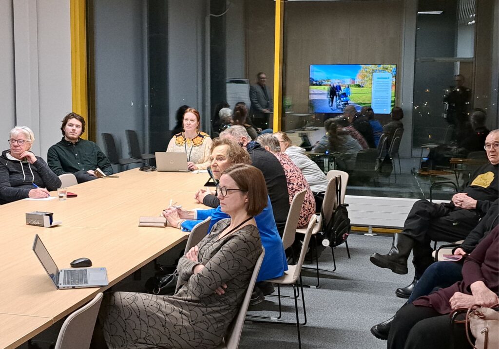 Ihmisiä pitkän pöydän ääressä, keskustelutilaisuus.