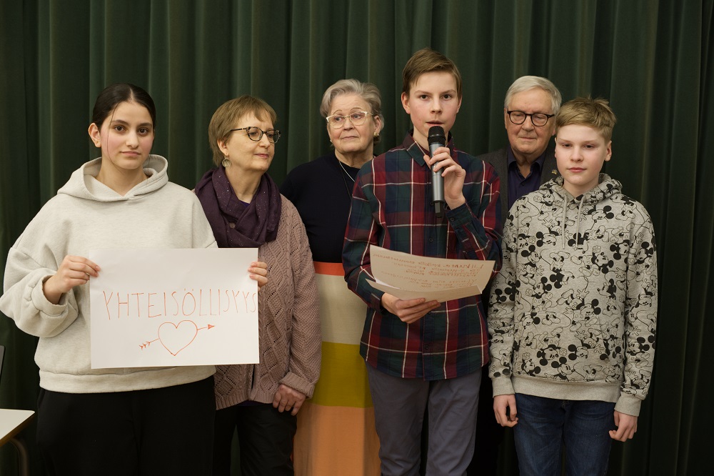 Kuusi eri-ikäistä vaikuttjaa vasemmalta oikealle: Malak Ateka pitelee käsissään kylttiä jossa lukee yhteisöllisyys, seuraavina Saija Vesanto, Liisa Majanen, Viljami Laakkonen, Pekka Raittila, Miika Kangas.