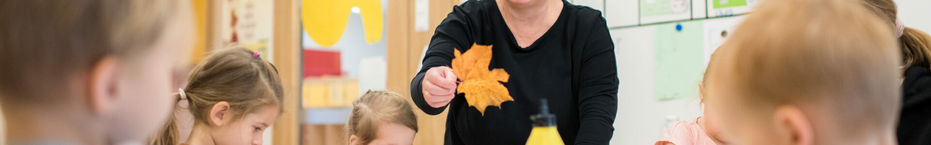 Luokkahuoneessa opettaja ja oppilaita. Opettajalla kädessään vaahteranlehti.