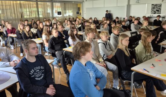 Joukko nuoria istumassa isossa salissa ja kuuntelemassa esitystä.
