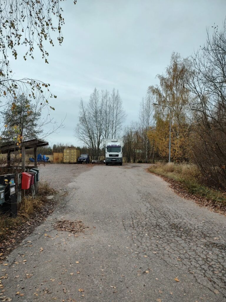 Kuorma-auto, maastoautoa, peräkärry ja kontteja tien päässä sijaitsevalla kääntöpaikalla.