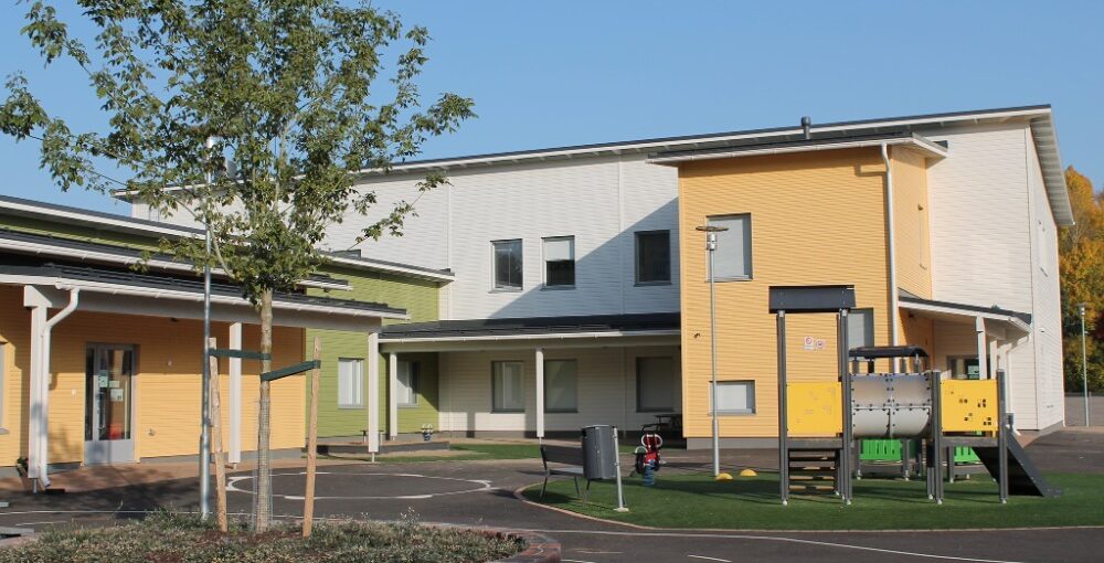 Saunakallion päiväkodin pihamaa, etualalla puu ja kiipeilyteline, päiväkotirakennus taustalla