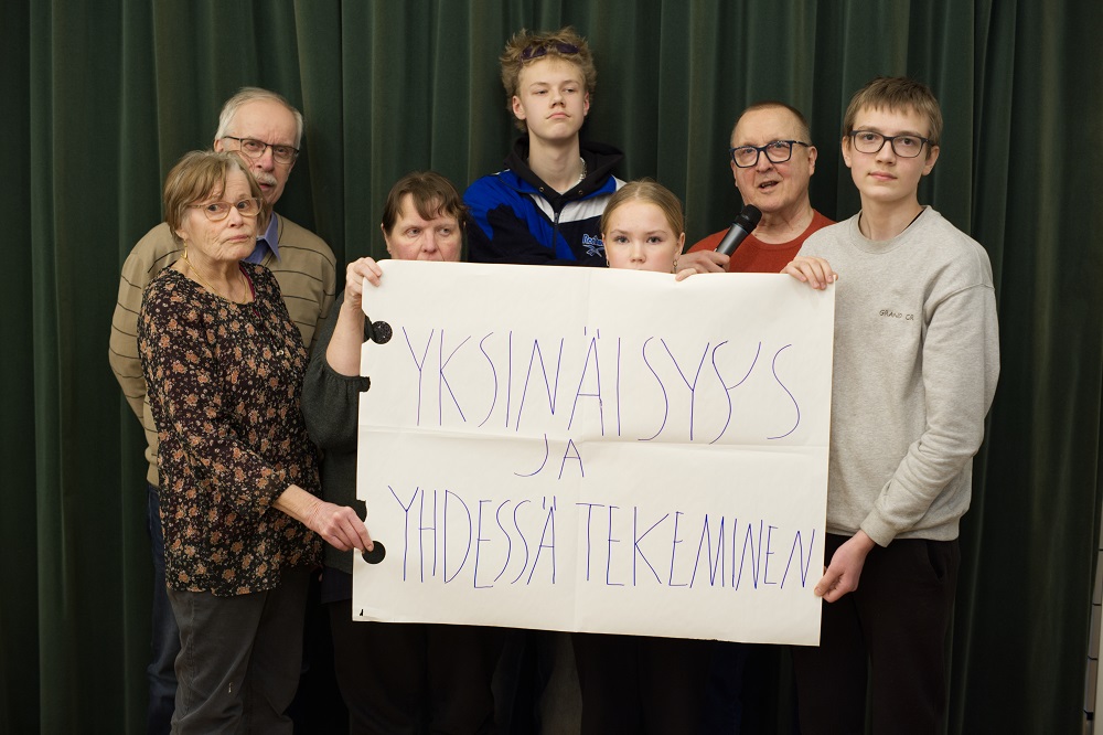 Kuvassa 7 vaikuttajaa (vasemmalta oikealle): Kaija Jaukkari, Esko Lappalainen, Irma Saari, Niilo Sipilä, Hilda Haverinen, Ossi Kaminen, Rauto Hautamäki. Kylttiä pidellään usean käden voimin ja kyltissä lukee Yksinäisyys ja yhdessä tekeminen.