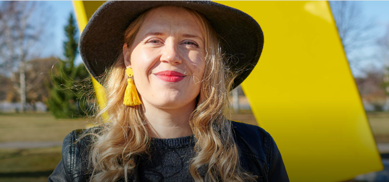 Hymyilevä nainen keltaisen Kolmisointu-patsaan edessä