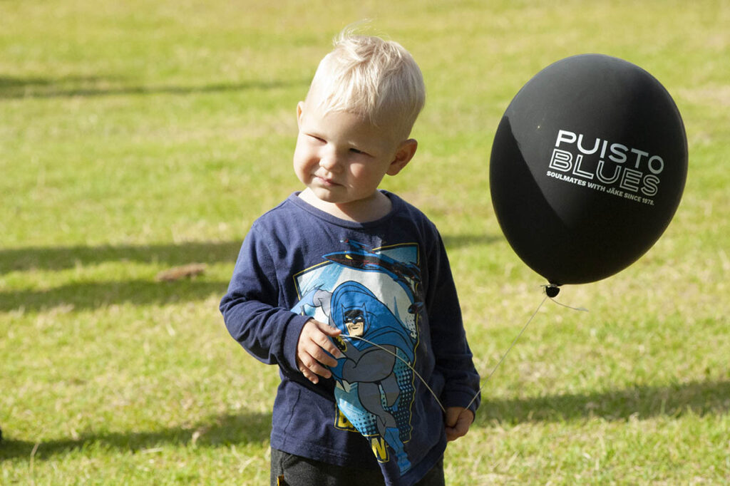 Nurmikolla pieni poika, jolla kädessä Puistoblues -ilmapallo.
