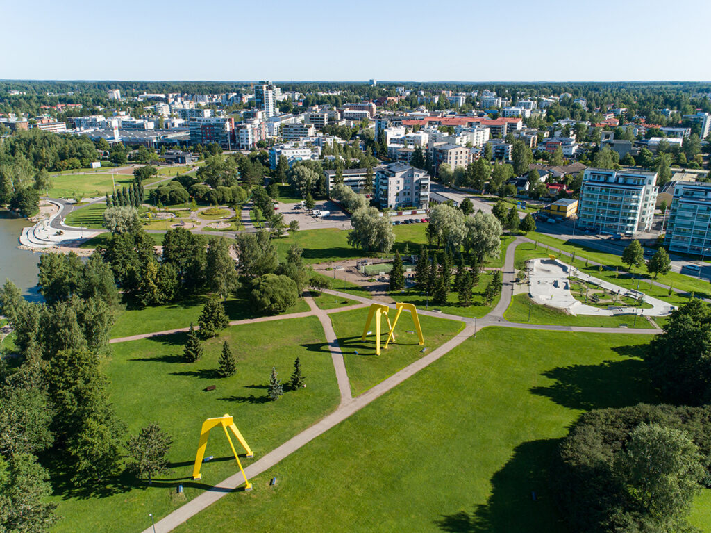 Ilmakuvassa kaupunkikuvaa, rakennuksia kuvan taka-alalla, puistoa etualalla.