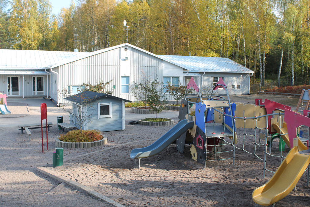 Nummenkylän päiväkodin pihamaa, etualalla kiipeilytelineitä, takana vaalea päiväkotirakennus