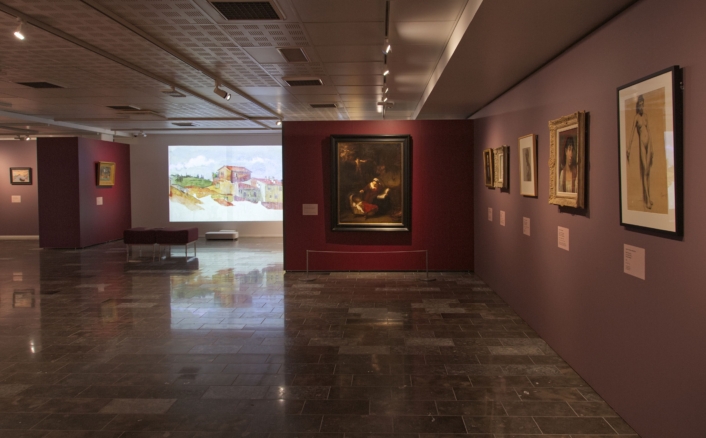 Taidegalleria, jossa on esillä useita maalauksia tummilla seinillä. Keskellä on suuri maalaus ja taustalla näkyy maisemaprojektio.