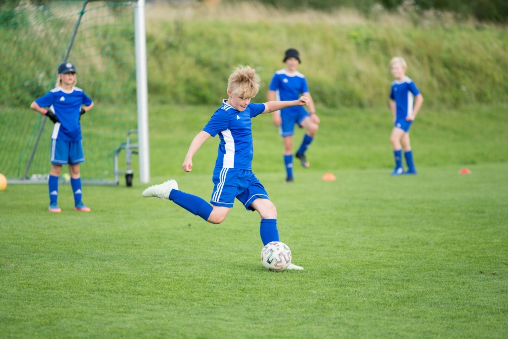 Jalkapalloileva lapsi vihreällä kentällä. Taustalla joukkuetovereita. Lasten ja nuorten harrastustuki voitti osallistuvan budjetoinnin 430 äänellä vuoden 2025 lopussa. Nyt tukisumma 10 000 euroa jaetaan vapaamuotoisten hakemusten pohjalta.