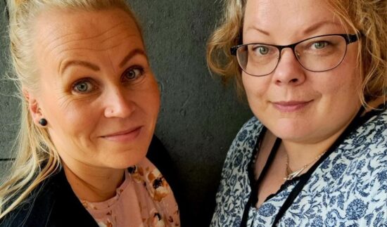 Kaksi vaaleahiuksista naista hymyilee kuvassa. Toisella henkilöllä on silmälasit päässä.